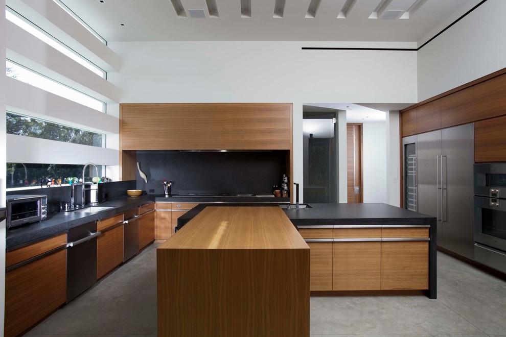 Design ideas for a large contemporary u-shaped kitchen in Los Angeles with an undermount sink, flat-panel cabinets, medium wood cabinets, black splashback, stainless steel appliances, concrete floors, multiple islands, grey floor, wood benchtops and black benchtop.