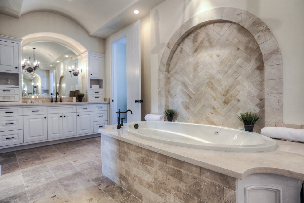 This is an example of a mid-sized mediterranean master bathroom in Houston with an undermount sink, raised-panel cabinets, white cabinets, limestone benchtops, a drop-in tub, an open shower, beige tile, stone tile, beige walls and travertine floors.