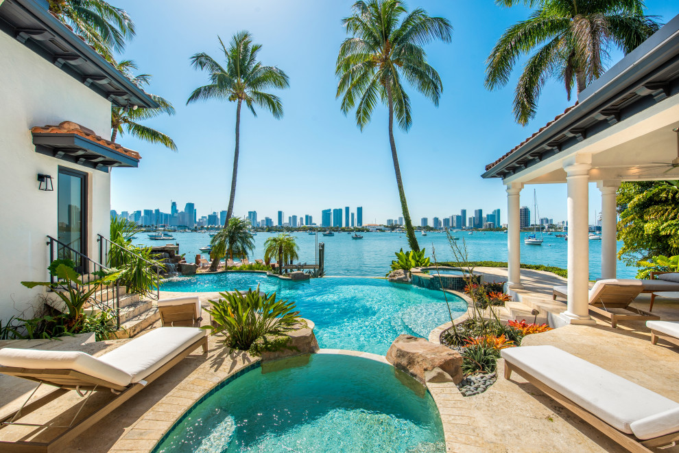 Large tropical side yard custom-shaped pool in Miami with a pool house and brick pavers.