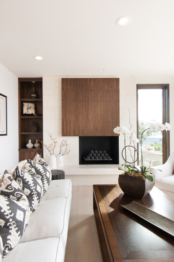This is an example of a modern living room in Orange County with white walls, light hardwood floors and a standard fireplace.