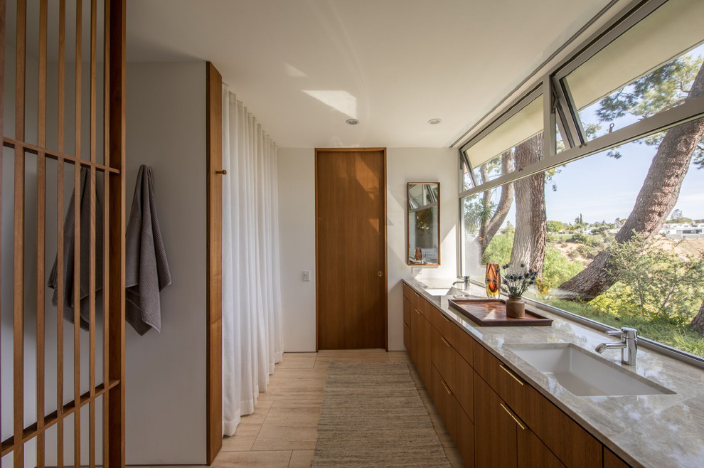 This is an example of a midcentury master bathroom in Los Angeles with flat-panel cabinets, medium wood cabinets, grey benchtops, white walls, an undermount sink and beige floor.