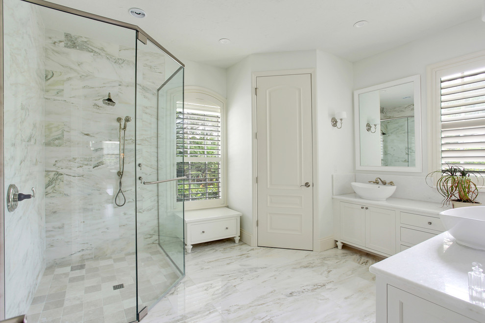This is an example of a transitional master bathroom in Tampa with white cabinets, white tile, stone tile, marble floors, a vessel sink, recessed-panel cabinets, a corner shower, white walls and a hinged shower door.