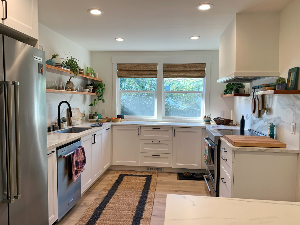 Photo of a mid-sized beach style u-shaped eat-in kitchen in San Francisco with an undermount sink, recessed-panel cabinets, white cabinets, solid surface benchtops, yellow splashback, stone slab splashback, stainless steel appliances, light hardwood floors, a peninsula, beige floor and yellow benchtop.