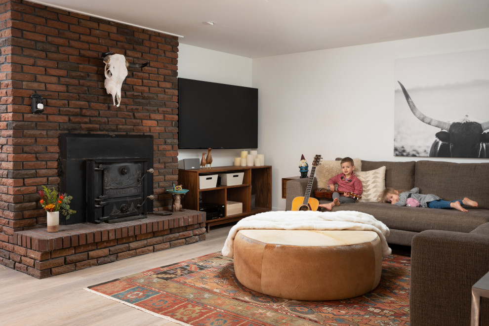 Photo of a modern walk-out basement in Denver with white walls, laminate floors, a wood stove and a brick fireplace surround.