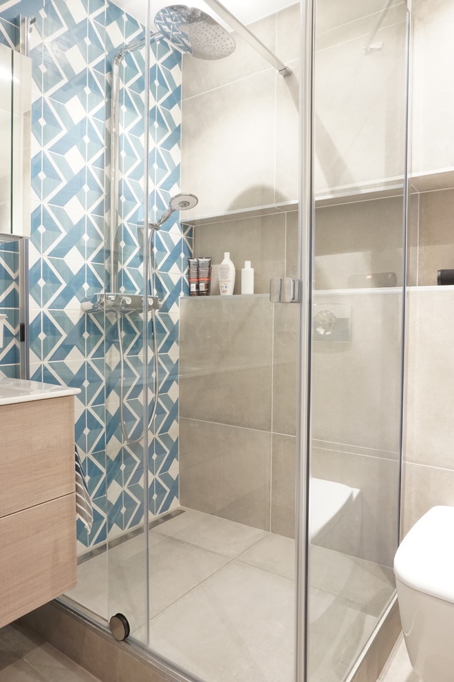 Large contemporary master bathroom in Paris with a curbless shower, a wall-mount toilet, blue tile, grey walls, an undermount sink, grey floor, a sliding shower screen and light wood cabinets.