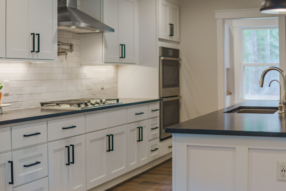 Foto på ett mellanstort lantligt kök, med en nedsänkt diskho, skåp i shakerstil, vita skåp, vitt stänkskydd, stänkskydd i keramik, rostfria vitvaror, mellanmörkt trägolv, en köksö och brunt golv