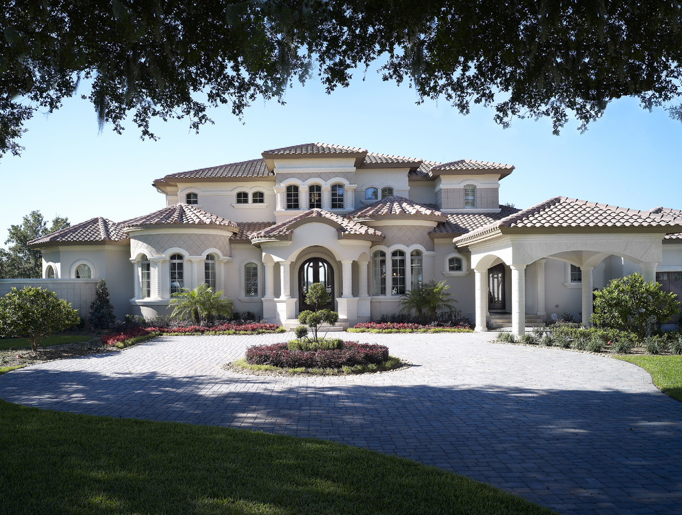This is an example of an expansive mediterranean two-storey stucco white house exterior in Tampa with a hip roof and a tile roof.