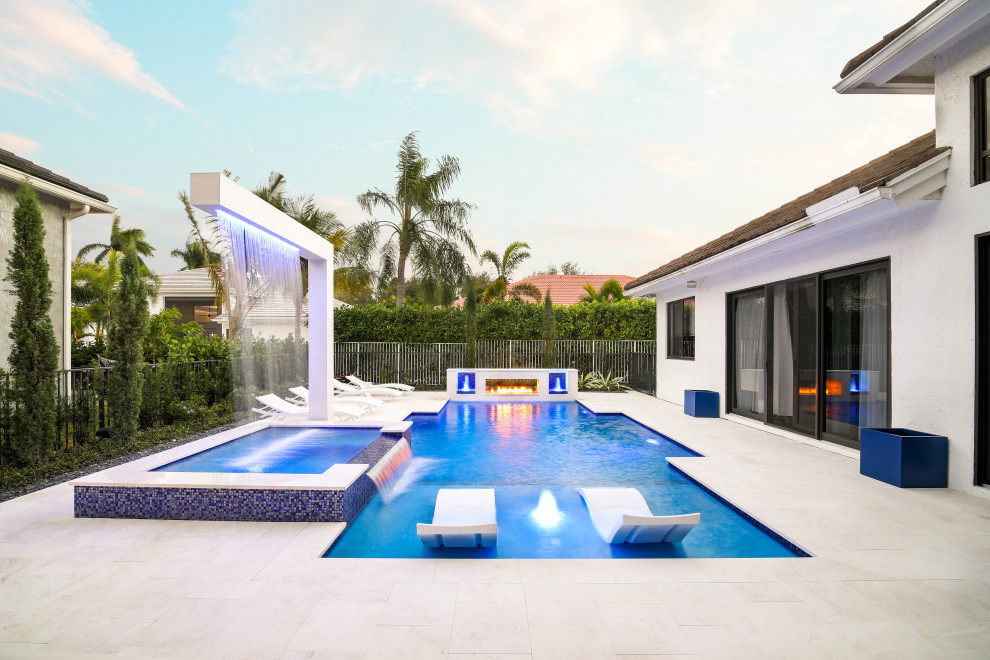This is an example of a large contemporary backyard custom-shaped lap pool in Miami with a hot tub and natural stone pavers.