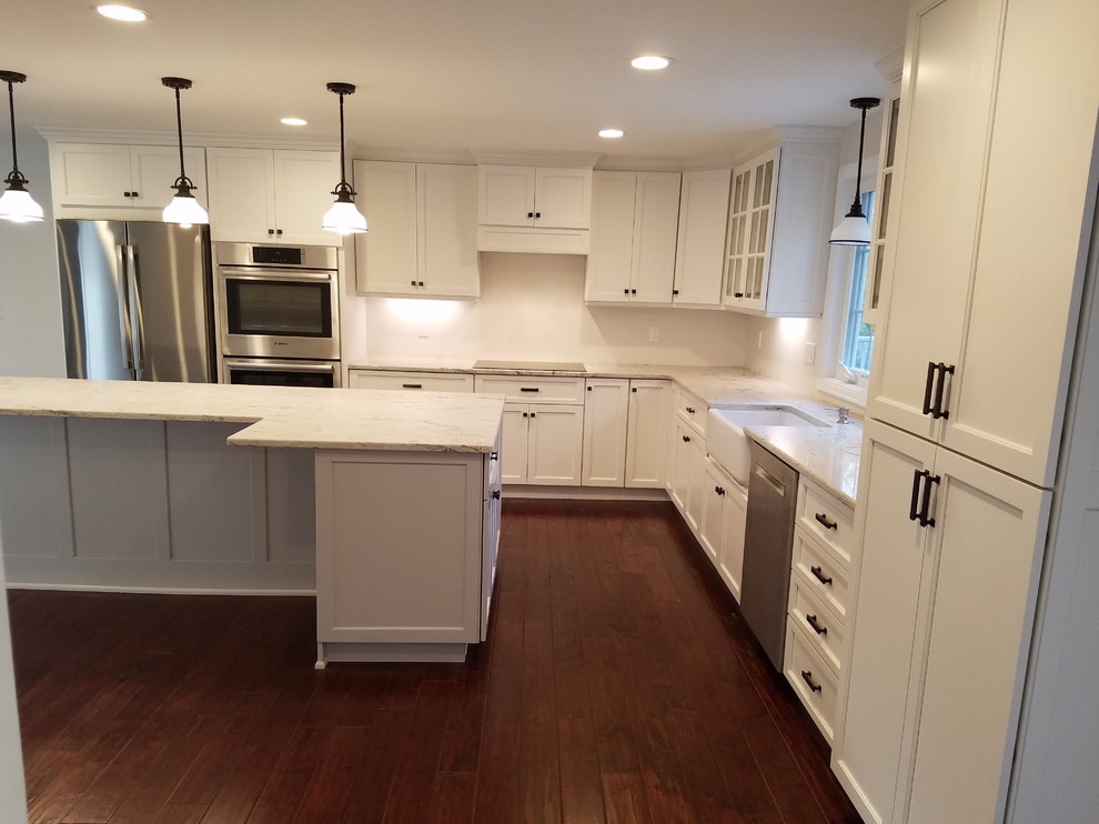 Example of a mid-sized transitional l-shaped dark wood floor and brown floor eat-in kitchen design with a farmhouse sink, shaker cabinets, white cabinets, granite countertops, white backsplash, subway tile backsplash, stainless steel appliances and an island