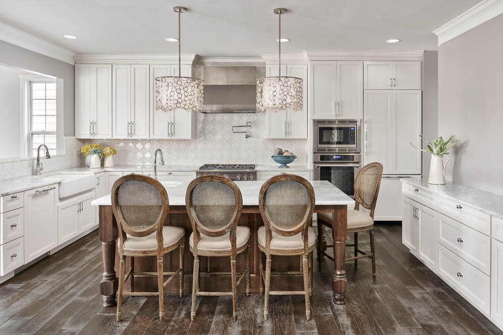 Design ideas for a large traditional u-shaped separate kitchen in DC Metro with a farmhouse sink, white cabinets, quartz benchtops, white splashback, ceramic splashback, stainless steel appliances, medium hardwood floors, with island and recessed-panel cabinets.
