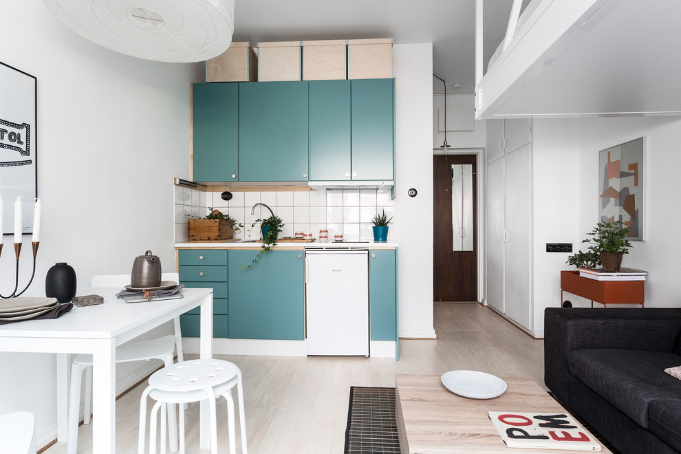 Photo of a small scandinavian single-wall open plan kitchen in Stockholm with flat-panel cabinets, turquoise cabinets, white splashback, white appliances, light hardwood floors, no island and beige floor.