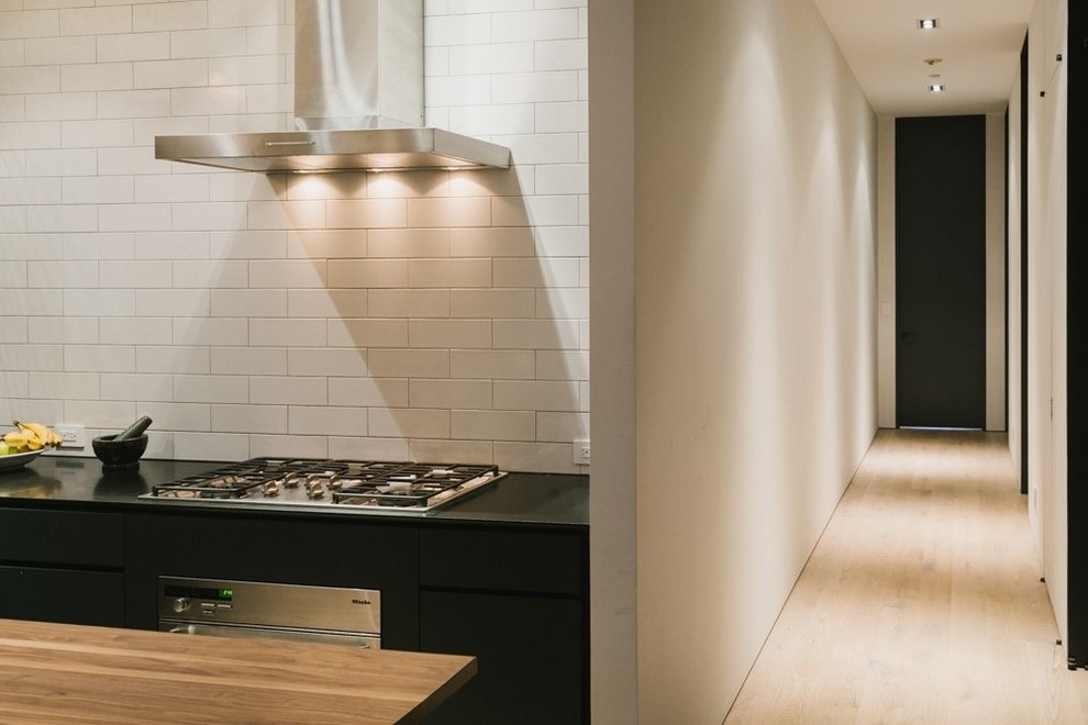Inspiration for a mid-sized contemporary u-shaped eat-in kitchen in New York with an undermount sink, flat-panel cabinets, black cabinets, marble benchtops, white splashback, subway tile splashback, stainless steel appliances, light hardwood floors and with island.