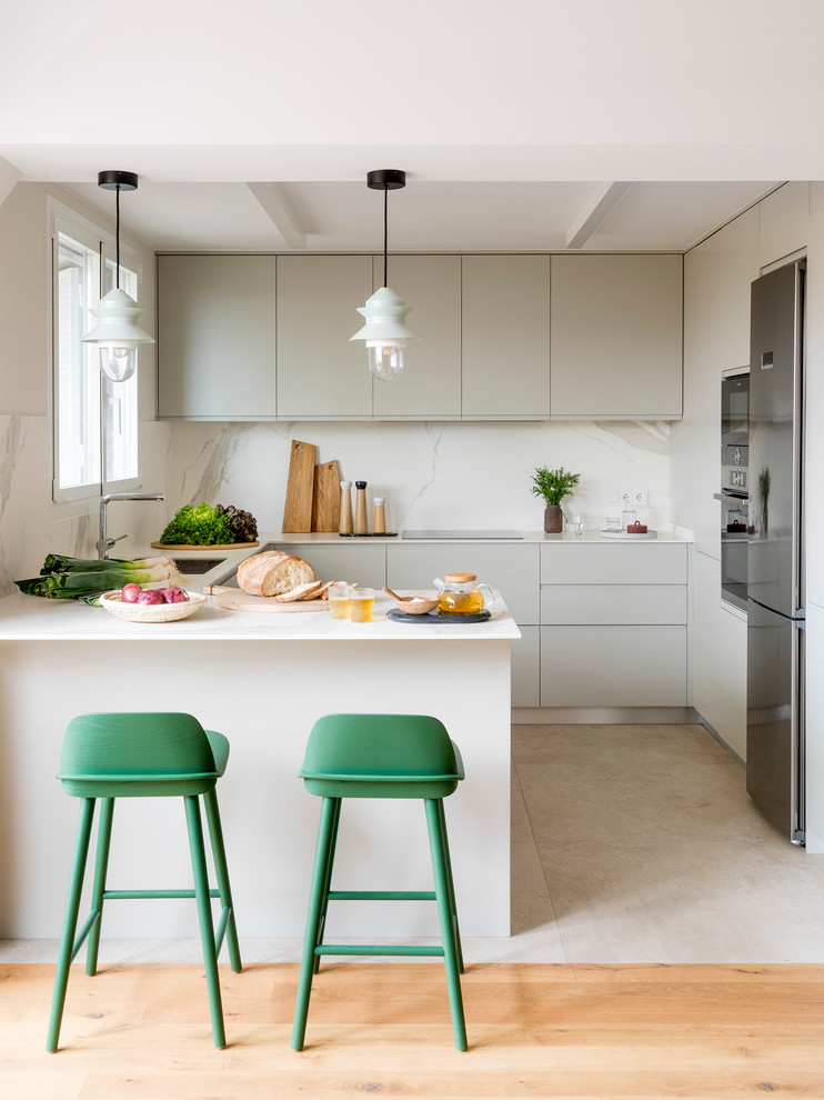 Inspiration for a mid-sized scandinavian u-shaped kitchen in Barcelona with flat-panel cabinets, grey cabinets, white splashback, a peninsula, a single-bowl sink, stone slab splashback, stainless steel appliances, beige floor and white benchtop.