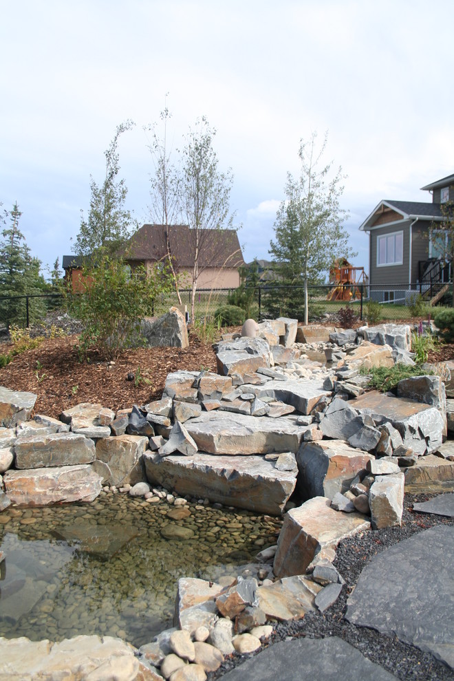 Design ideas for a traditional backyard full sun garden in Calgary with a water feature and natural stone pavers.