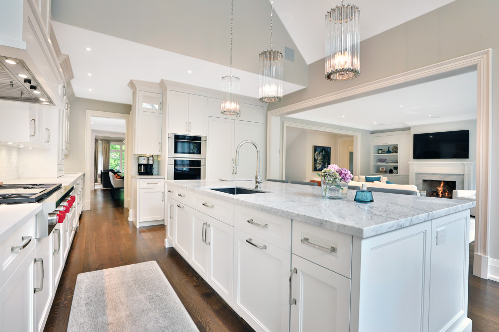 Example of a large transitional l-shaped medium tone wood floor and brown floor kitchen pantry design in Toronto with an undermount sink, shaker cabinets, white cabinets, quartz countertops, white backsplash, marble backsplash, paneled appliances, an island and white countertops