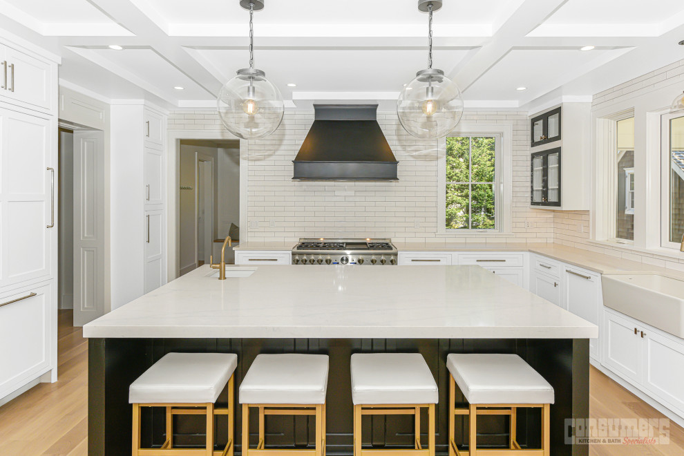 This is an example of a large midcentury l-shaped eat-in kitchen with a farmhouse sink, recessed-panel cabinets, white cabinets, quartz benchtops, white splashback, subway tile splashback, stainless steel appliances, medium hardwood floors, with island, brown floor, grey benchtop and exposed beam.