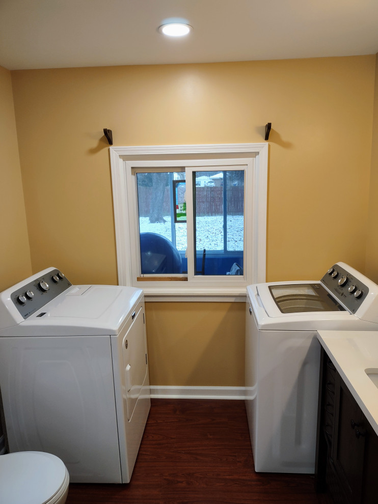 This is an example of a mid-sized traditional single-wall utility room in Detroit with an integrated sink, recessed-panel cabinets, dark wood cabinets, laminate benchtops, orange walls, laminate floors, an integrated washer and dryer, brown floor and beige benchtop.