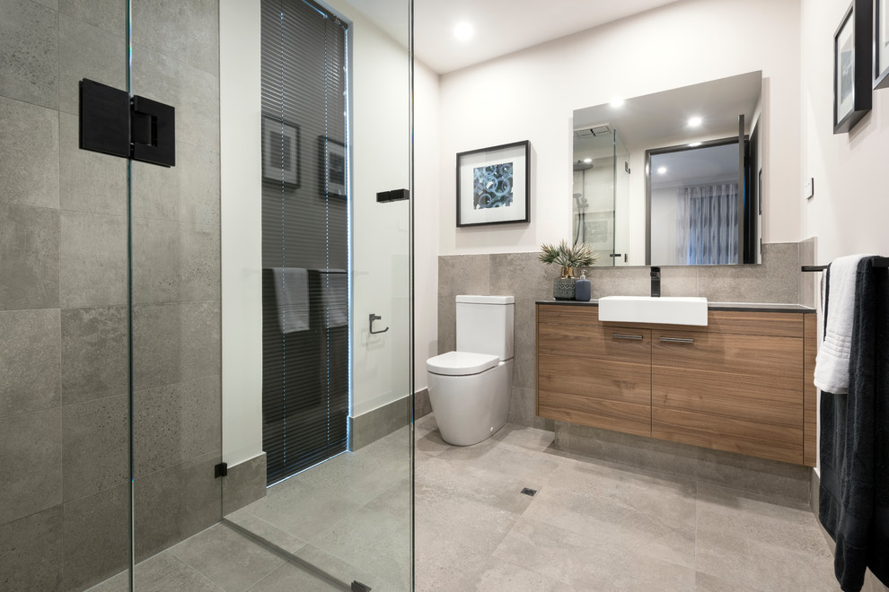 This is an example of a contemporary 3/4 bathroom in Perth with flat-panel cabinets, medium wood cabinets, a corner shower, gray tile, white walls, a drop-in sink, grey floor and a hinged shower door.