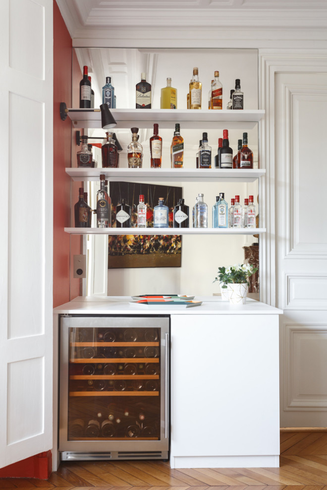 Photo of a small modern single-wall home bar in Paris with no sink, flat-panel cabinets, white cabinets, laminate benchtops, grey splashback, mirror splashback, medium hardwood floors, brown floor and white benchtop.