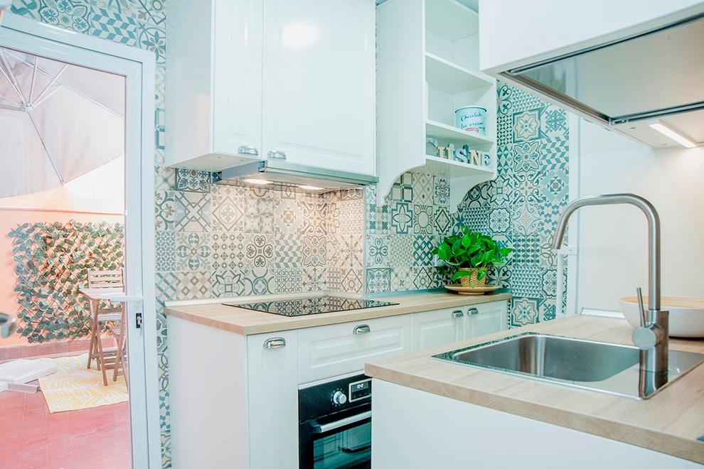 Photo of a small scandinavian kitchen in Madrid with beaded inset cabinets, white cabinets, wood benchtops, multi-coloured splashback, white appliances, porcelain floors and brown benchtop.