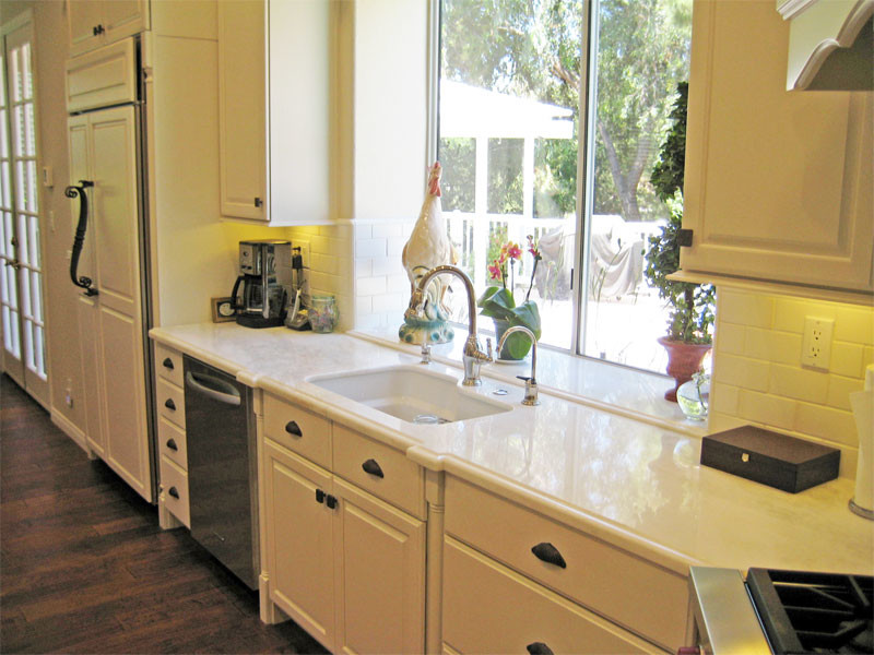 Mid-sized transitional u-shaped dark wood floor and brown floor enclosed kitchen photo in Orange County with an undermount sink, raised-panel cabinets, white cabinets, solid surface countertops, white backsplash, subway tile backsplash, stainless steel appliances and an island