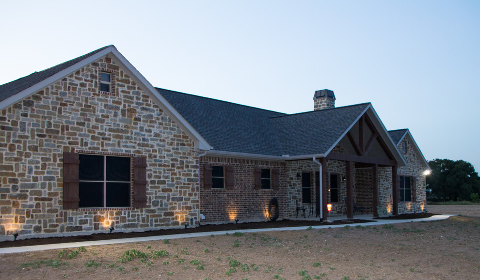 Photo of a mid-sized country one-storey brown house exterior in Dallas with stone veneer, a gable roof and a shingle roof.