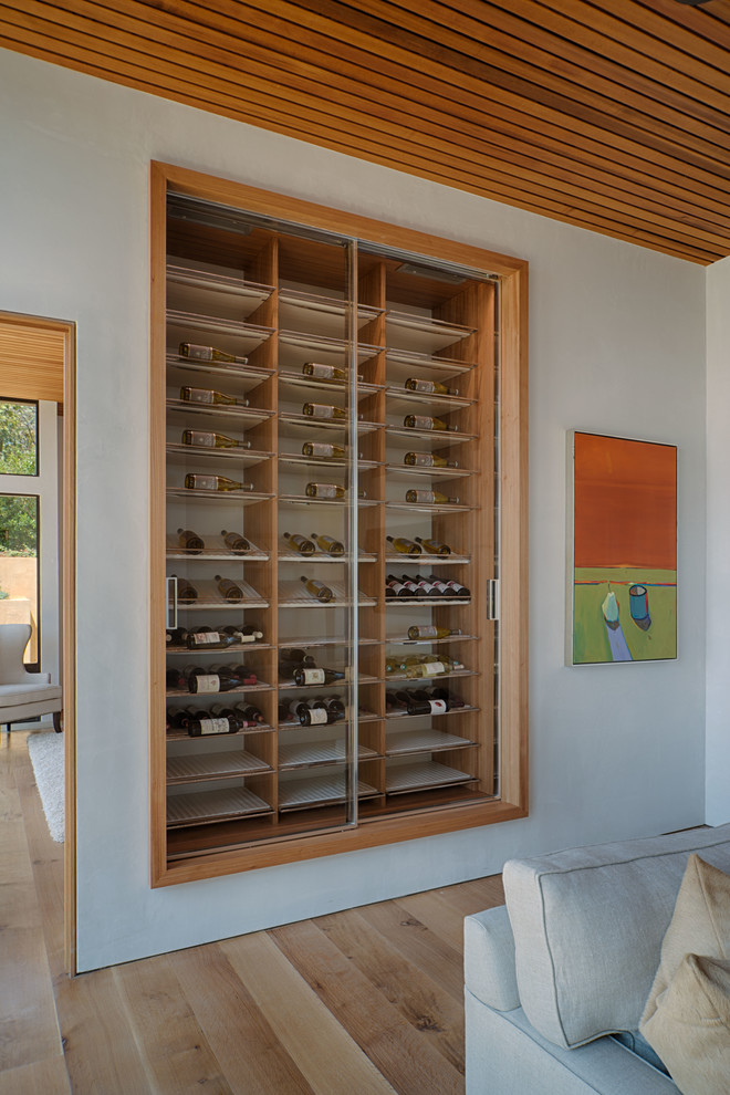 This is an example of a small contemporary wine cellar in San Francisco with light hardwood floors and display racks.