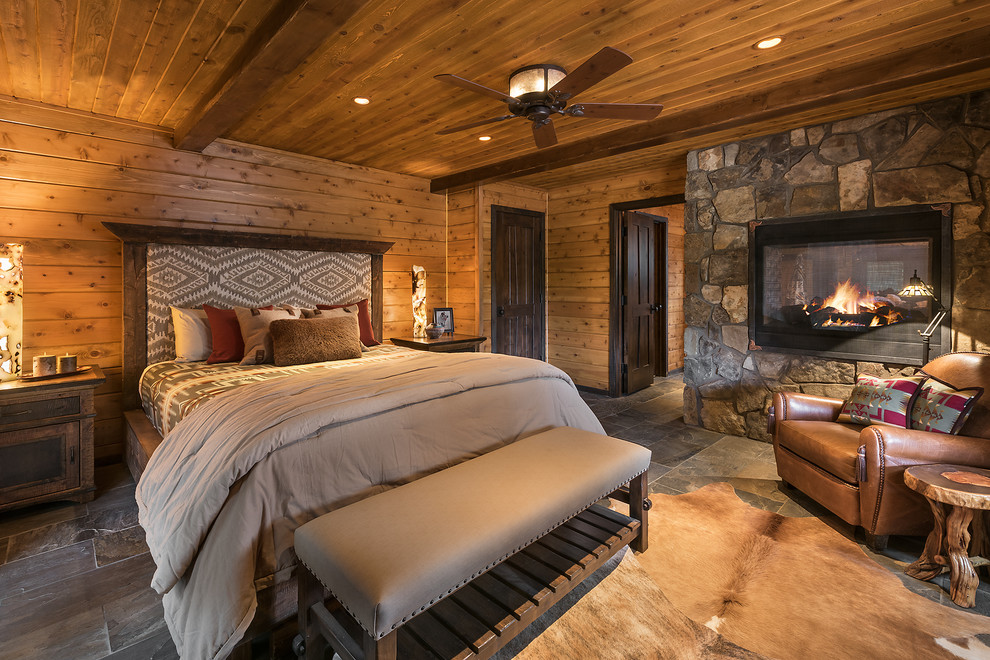 Design ideas for a large country master bedroom in Phoenix with slate floors, a two-sided fireplace, a stone fireplace surround, brown walls and grey floor.