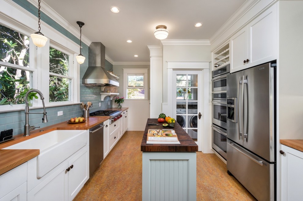 Inspiration for a traditional galley kitchen in Portland with a farmhouse sink, shaker cabinets, white cabinets, wood benchtops, grey splashback, subway tile splashback, stainless steel appliances and with island.