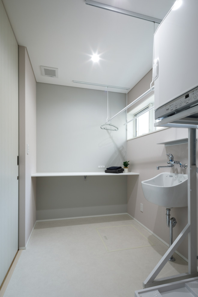 Photo of a scandinavian single-wall utility room in Other with white walls, a stacked washer and dryer, white floor, white benchtop, wallpaper, wallpaper, an utility sink, laminate benchtops and linoleum floors.