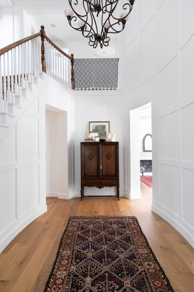 Idee per un grande ingresso classico con pareti bianche, pavimento in legno massello medio, pavimento marrone e pannellatura