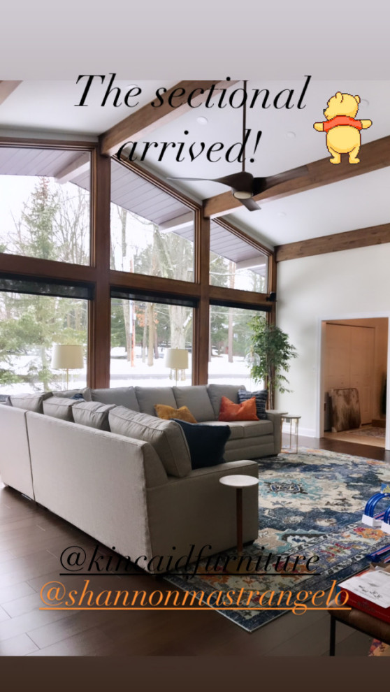 Design ideas for an expansive midcentury enclosed living room in Other with white walls, medium hardwood flooring, a standard fireplace, a stone fireplace surround, a wall mounted tv, brown floors and exposed beams.