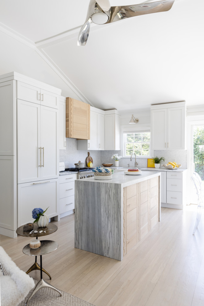 Photo of a beach style l-shaped kitchen in New York with a belfast sink, shaker cabinets, white cabinets, light hardwood flooring, an island, beige floors, white worktops and a vaulted ceiling.