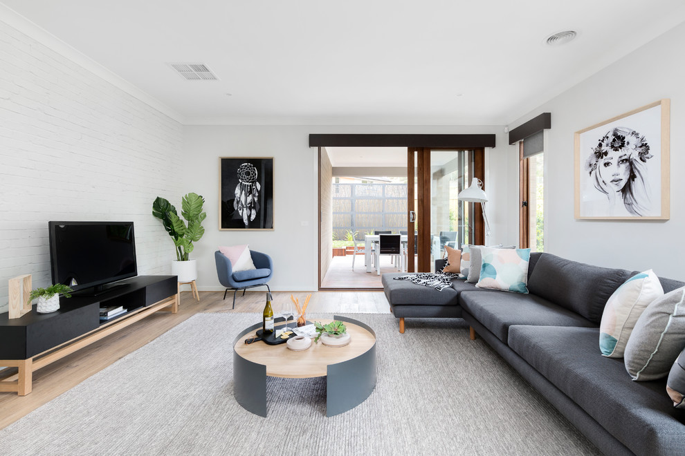 Scandinavian living room in Melbourne with grey walls, light hardwood floors and a freestanding tv.