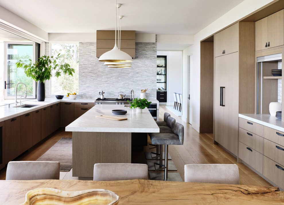 Contemporary u-shaped eat-in kitchen in San Francisco with a single-bowl sink, flat-panel cabinets, medium wood cabinets, quartzite benchtops, stainless steel appliances, medium hardwood floors, with island, white benchtop, grey splashback, matchstick tile splashback and brown floor.