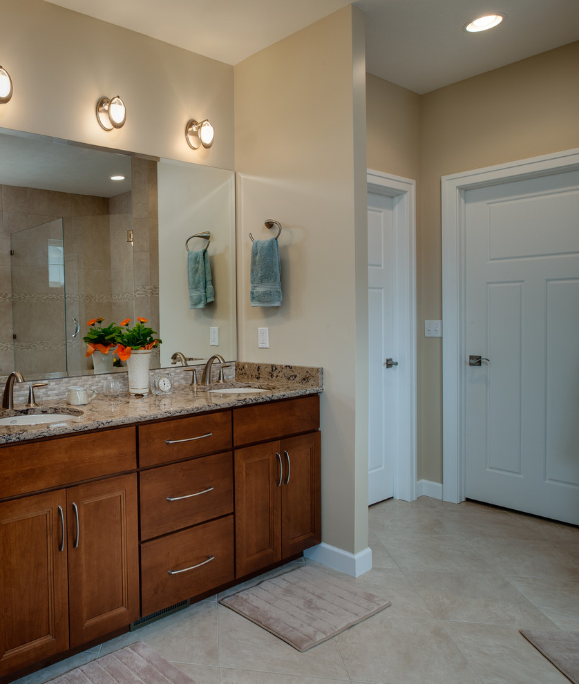Example of a large transitional master beige tile and stone tile porcelain tile bathroom design with an undermount sink, recessed-panel cabinets, medium tone wood cabinets, granite countertops and beige walls