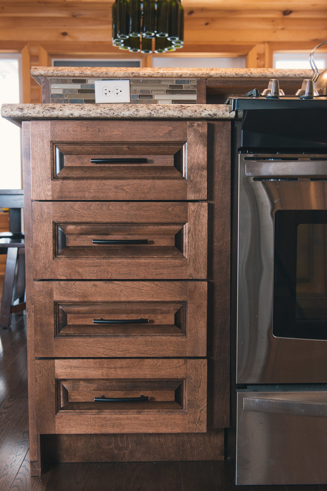 Example of a mid-sized mountain style l-shaped dark wood floor and brown floor home design design with raised-panel cabinets, medium tone wood cabinets, laminate countertops, multicolored backsplash, stainless steel appliances, a peninsula and beige countertops