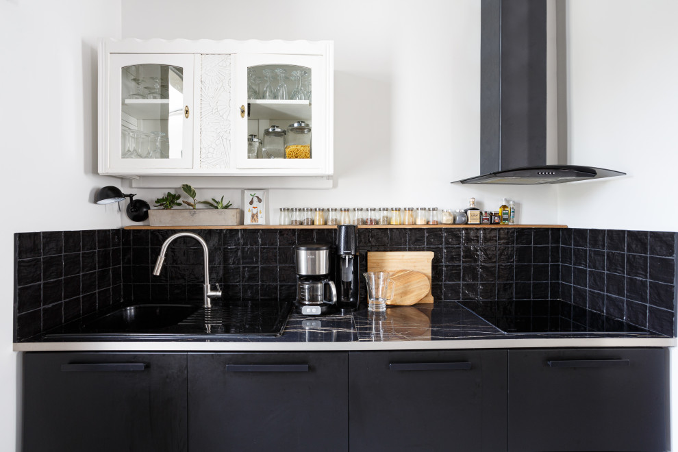Mid-sized eclectic galley open plan kitchen in Paris with a single-bowl sink, beaded inset cabinets, black cabinets, tile benchtops, black splashback, terra-cotta splashback, panelled appliances, concrete floors, with island, grey floor and black benchtop.
