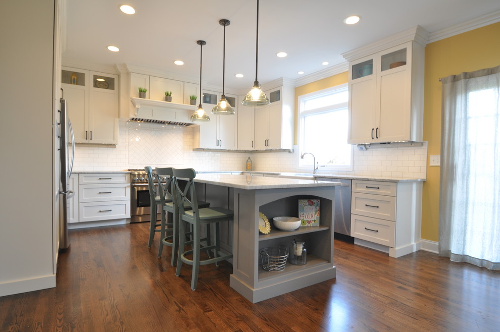 Inspiration for a large transitional medium tone wood floor eat-in kitchen remodel in Chicago with a farmhouse sink, shaker cabinets, white cabinets, marble countertops, white backsplash, subway tile backsplash, stainless steel appliances and an island