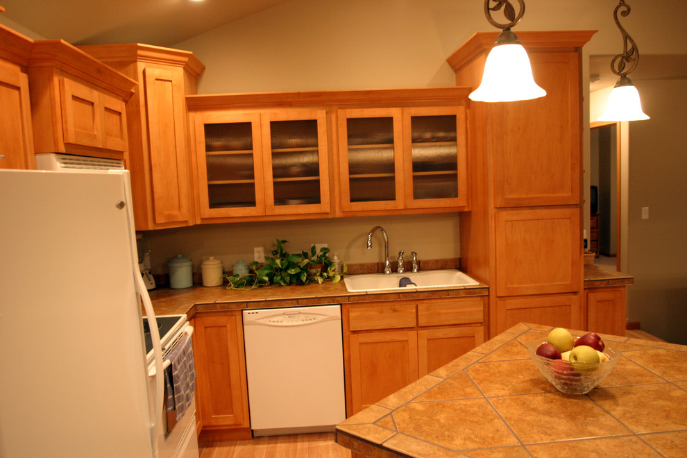 Example of a small l-shaped open concept kitchen design with shaker cabinets, light wood cabinets, tile countertops, white appliances and an island