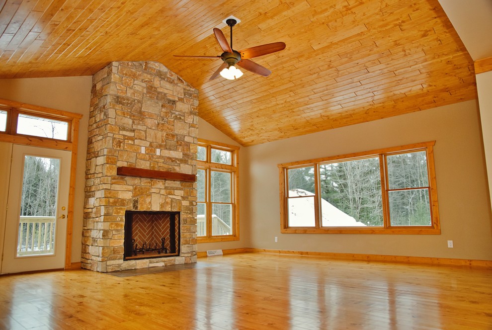 Example of a large mountain style open concept light wood floor and brown floor home design design with beige walls, a wood stove and a stone fireplace