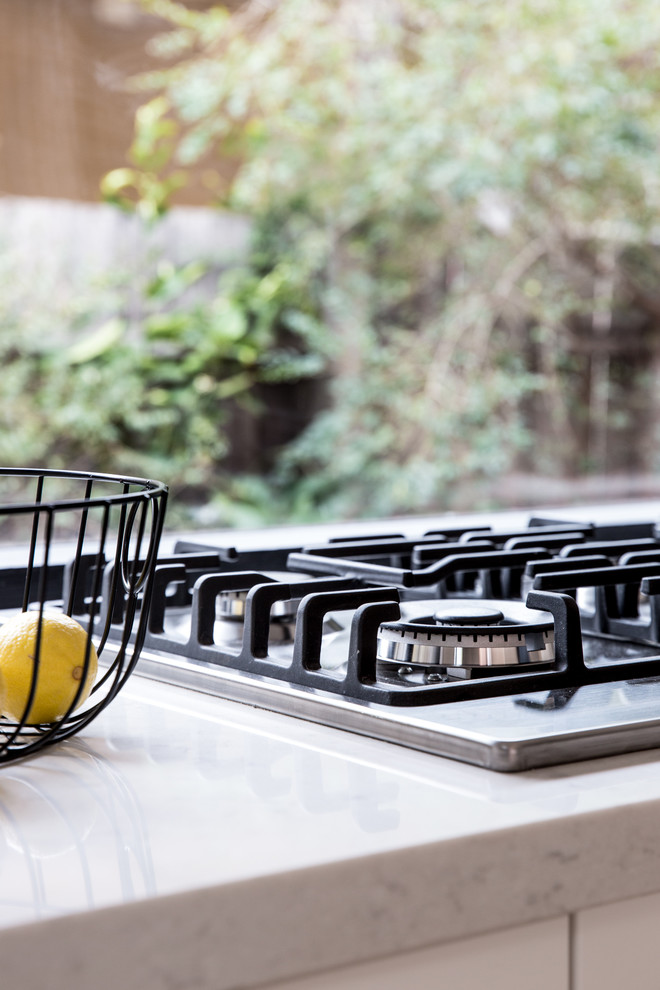 Photo of a large traditional single-wall eat-in kitchen in Melbourne with an undermount sink, flat-panel cabinets, white cabinets, quartz benchtops, glass sheet splashback, stainless steel appliances, light hardwood floors and no island.