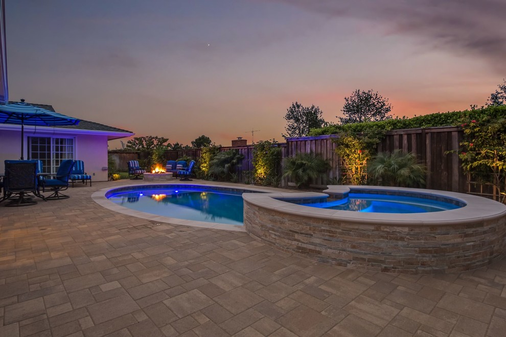 This is an example of a mid-sized transitional backyard round lap pool in Orange County with a hot tub and natural stone pavers.