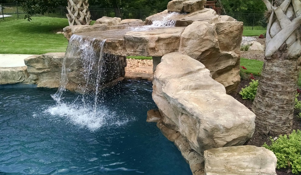 Large tropical backyard custom-shaped pool in Charlotte with a water feature and natural stone pavers.