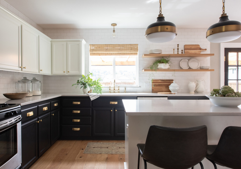 This is an example of a country l-shaped kitchen in Seattle with shaker cabinets, black cabinets, stainless steel appliances, light hardwood floors, with island, brown floor, white benchtop, white splashback and subway tile splashback.