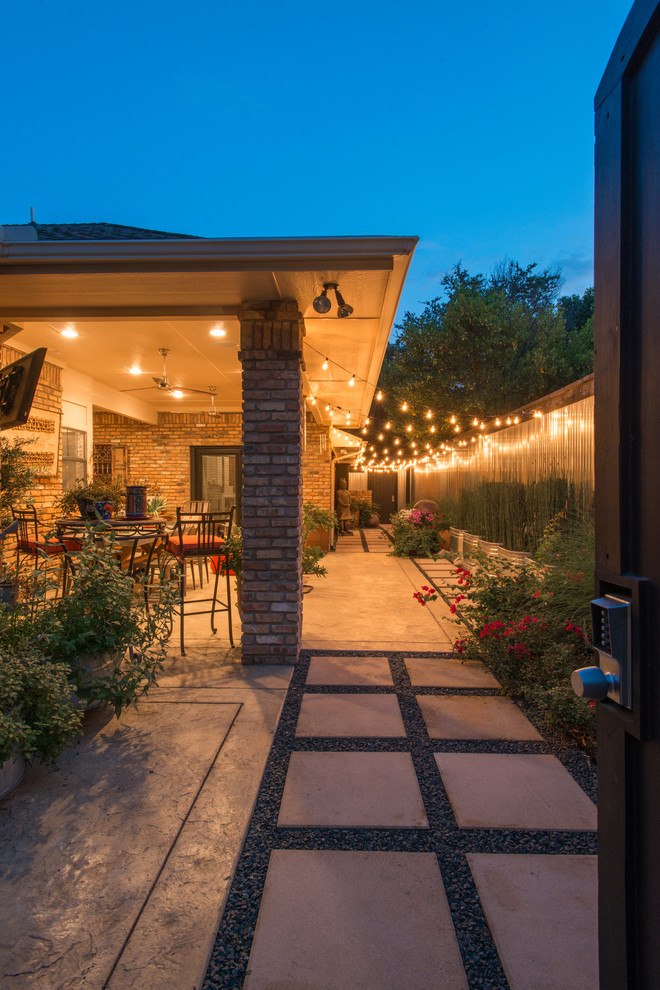 This is an example of a small eclectic side yard patio in Dallas with a container garden, stamped concrete and a roof extension.