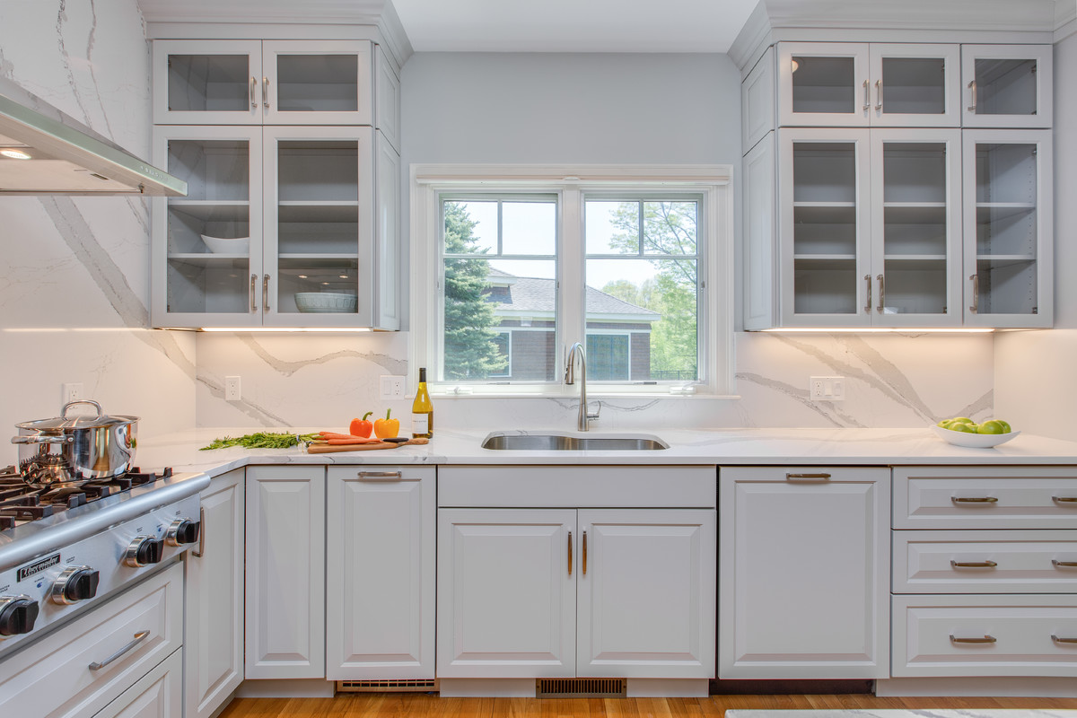 Large transitional l-shaped medium tone wood floor open concept kitchen photo in Boston with an undermount sink, raised-panel cabinets, gray cabinets, quartz countertops, stone slab backsplash, paneled appliances and an island
