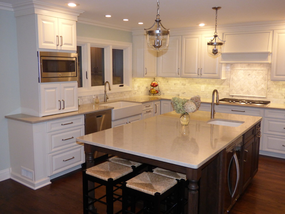 Eat-in kitchen - large transitional u-shaped dark wood floor eat-in kitchen idea in Chicago with a farmhouse sink, raised-panel cabinets, white cabinets, quartz countertops, gray backsplash, stone tile backsplash, stainless steel appliances and an island