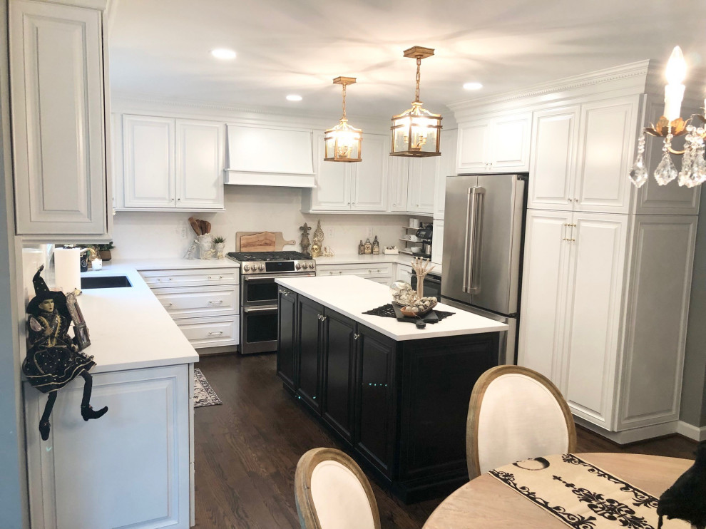 Photo of a mid-sized traditional u-shaped eat-in kitchen in Detroit with an undermount sink, raised-panel cabinets, white cabinets, quartz benchtops, white splashback, engineered quartz splashback, stainless steel appliances, dark hardwood floors, with island, brown floor and white benchtop.