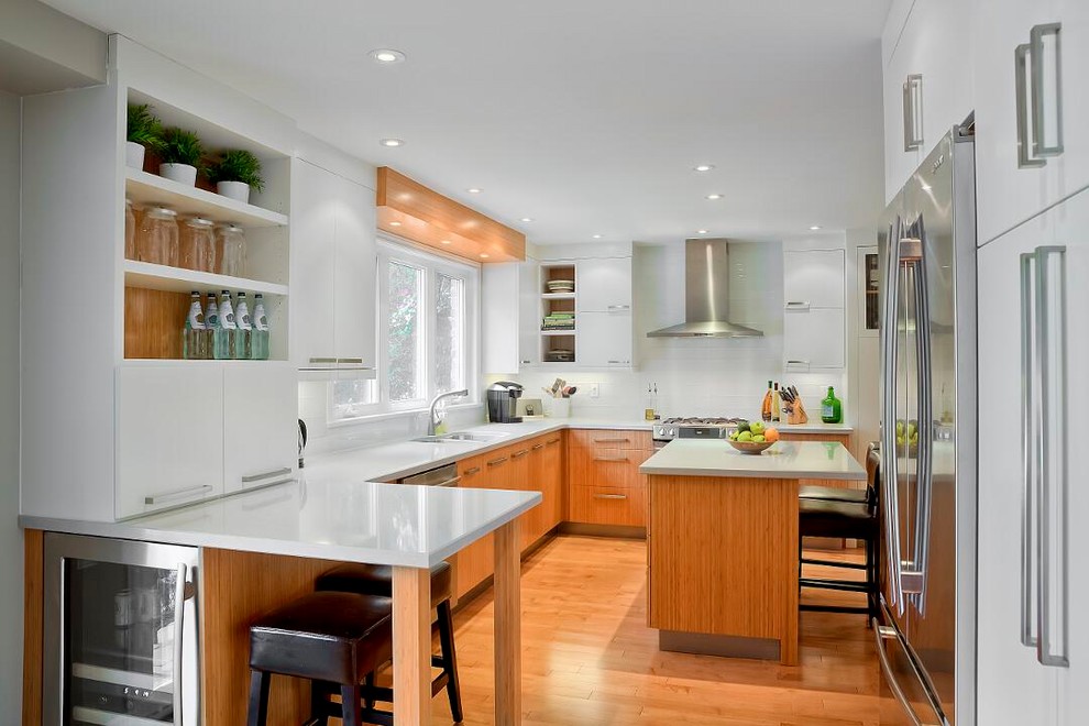 Contemporary l-shaped kitchen in Boston with flat-panel cabinets, white cabinets, white splashback, stainless steel appliances, medium hardwood floors, with island and brown floor.
